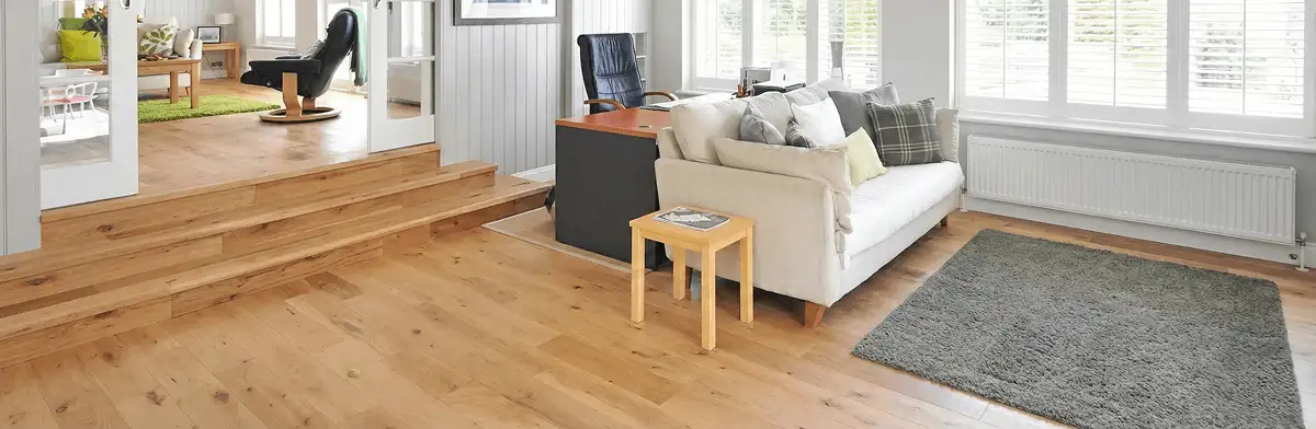 A modern living room with professionally installed laminate flooring, a beige sofa, a small side table, a gray rug, and large windows with white shutters in Huntsville, AL